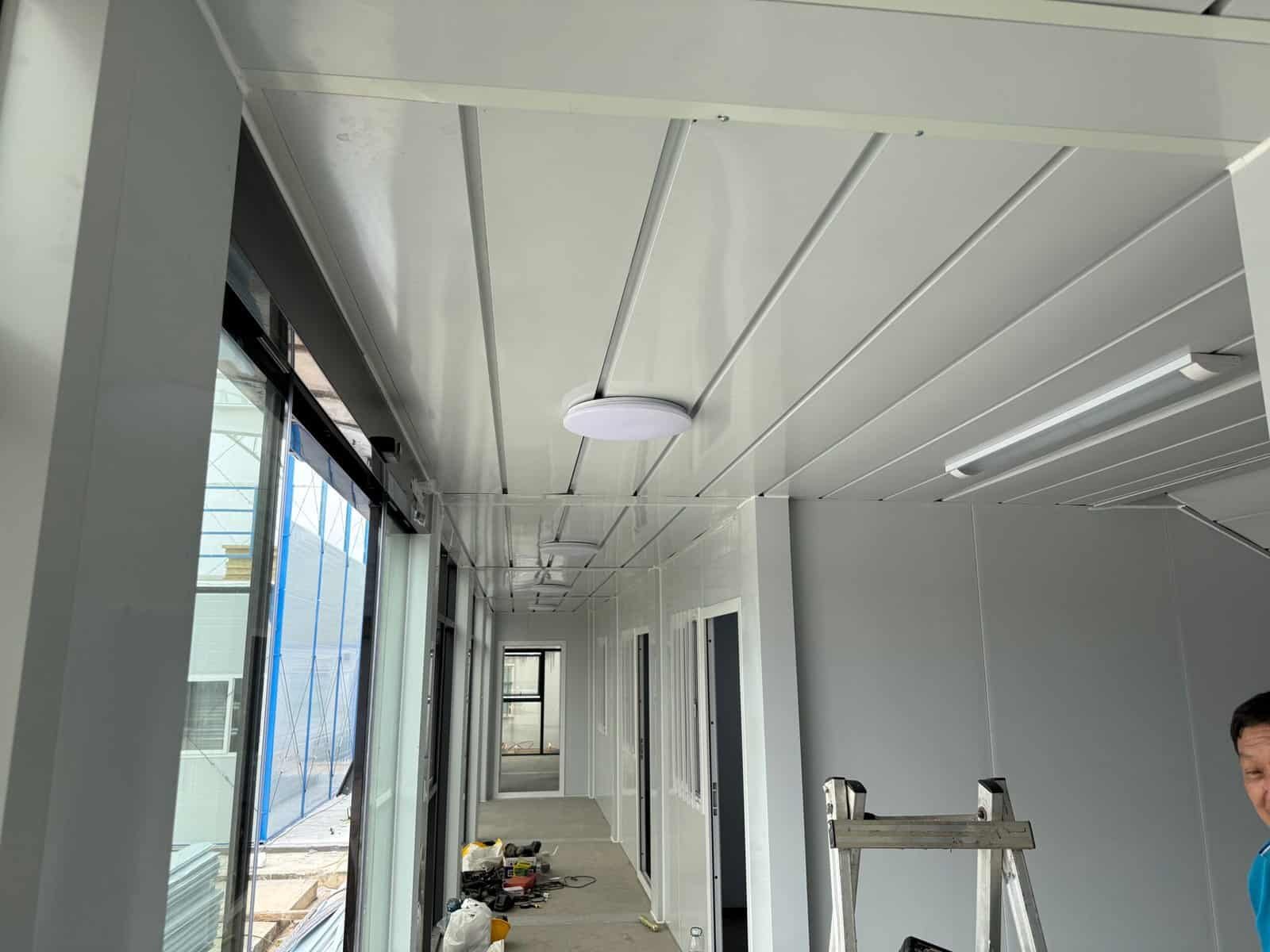 High-quality modular prefab office interior with white walls, ceiling panels, large windows, and modern lighting, showcasing efficient design and construction for commercial or residential use.