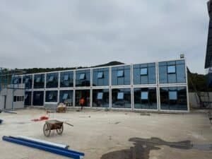 Modern modular prefab building with glass exterior, construction site with workers, ideal for scalable and sustainable housing or commercial spaces.