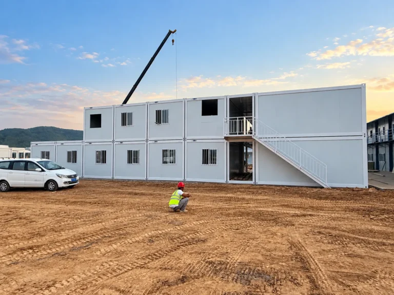 Crane assembling a two-story white modular building with an exterior metal staircase.