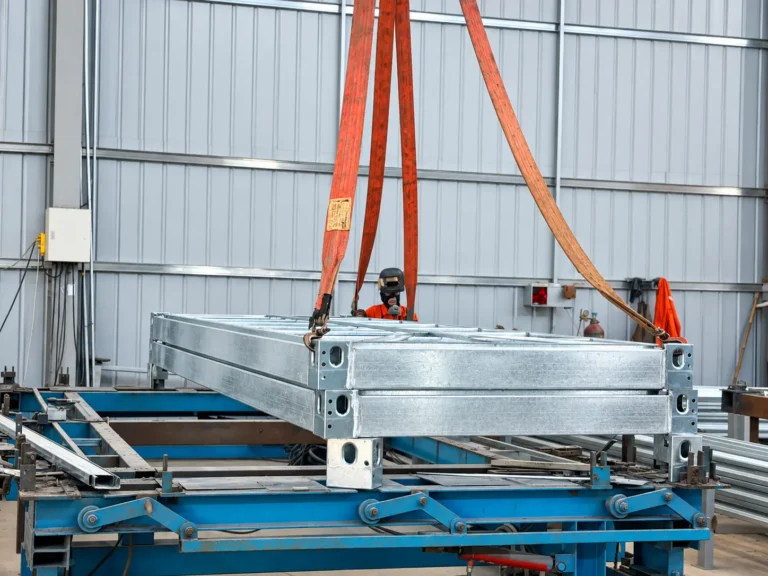Steel modular frames suspended from lifting straps above workshop fabrication equipment