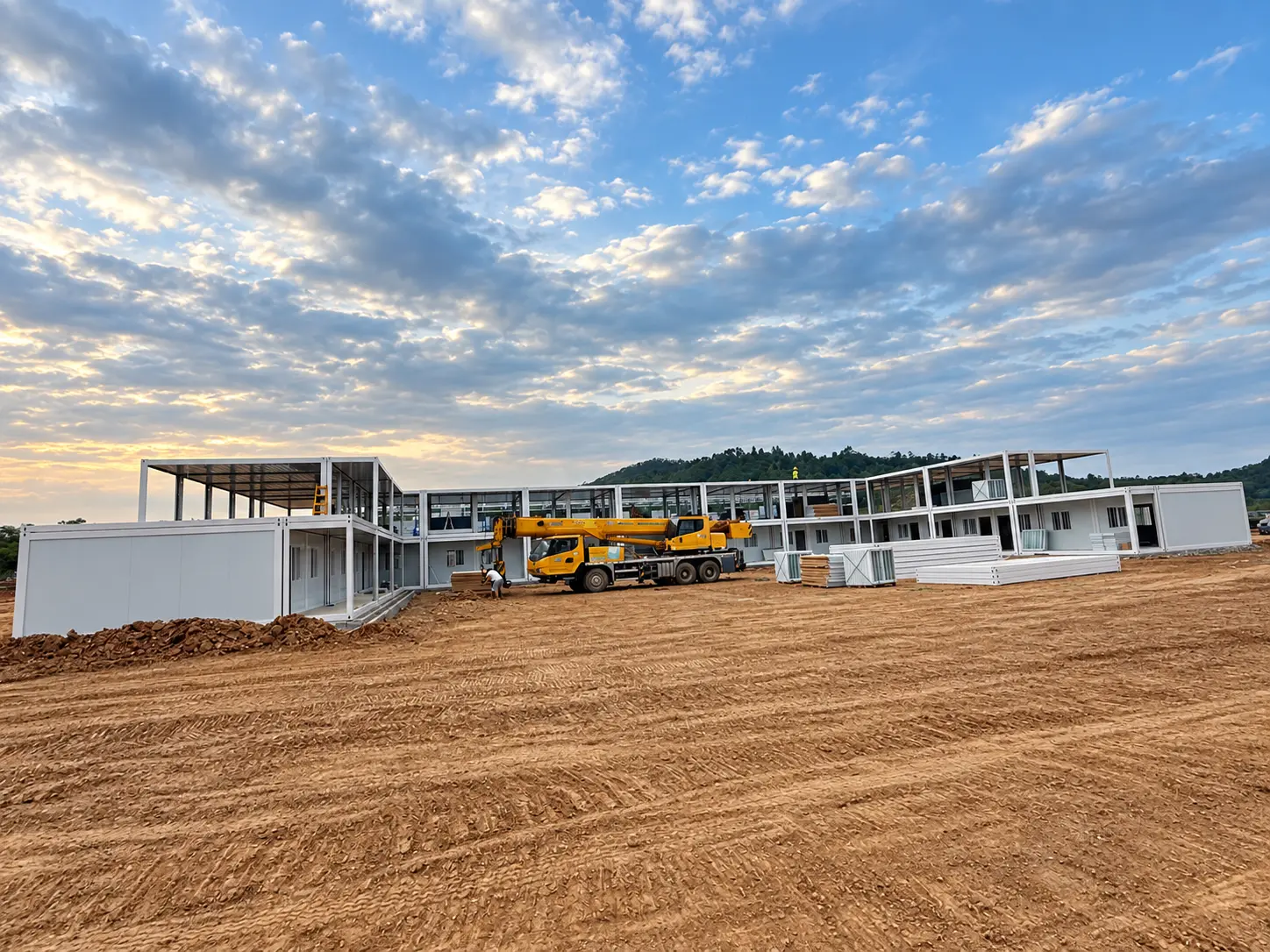 Wide construction-site view of a large modular building project with a mobile crane and prefabricated units.