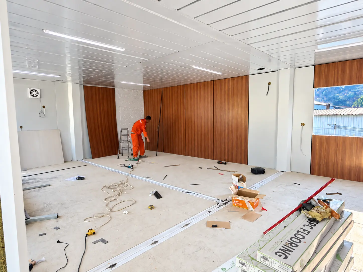 Worker fitting out a modular interior with wood-look wall panels and ceiling lighting
